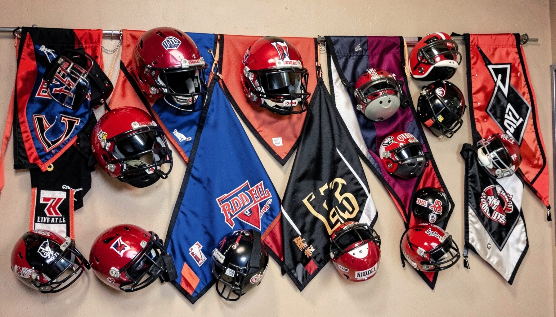 A display of Riddell mini helmets and team pennants arranged on a wall, bold team colors of red, blue, and black.